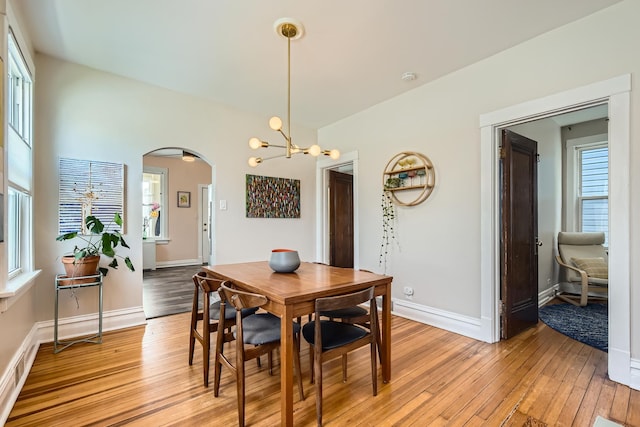 dining space featuring arched walkways, baseboards, a notable chandelier, and light wood-style floors