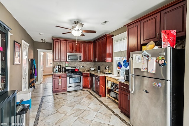 kitchen with reddish brown cabinets, light stone counters, stainless steel appliances, decorative backsplash, and ceiling fan