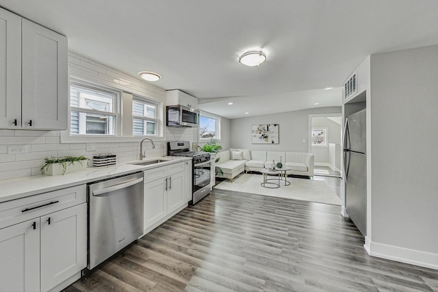 kitchen with tasteful backsplash, wood finished floors, stainless steel appliances, white cabinetry, and a sink