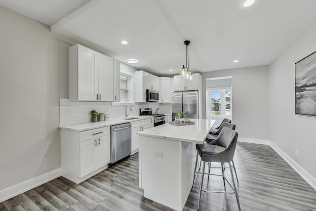 kitchen with wood finished floors, a sink, appliances with stainless steel finishes, tasteful backsplash, and a kitchen bar