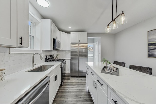 kitchen with pendant lighting, appliances with stainless steel finishes, dark wood-type flooring, white cabinets, and a sink