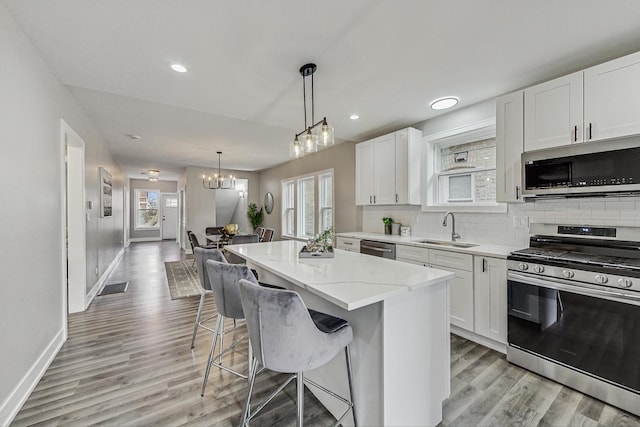 kitchen with a center island, a sink, stainless steel appliances, white cabinetry, and backsplash