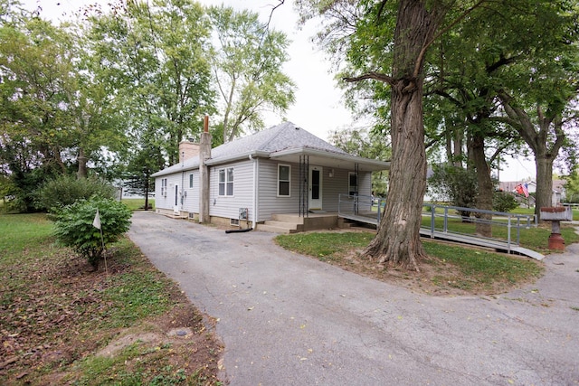 view of front facade with a porch, a chimney, a shingled roof, and aphalt driveway