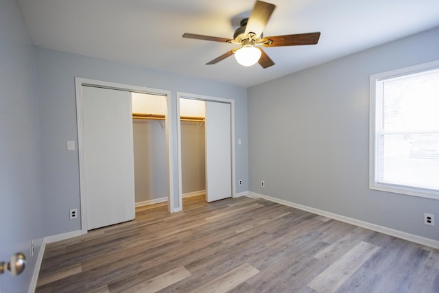 unfurnished bedroom with ceiling fan, baseboards, two closets, and wood finished floors