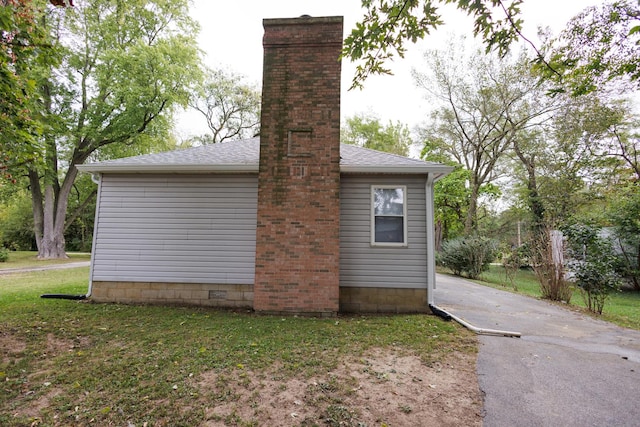 view of side of home with a shingled roof, a chimney, and a yard