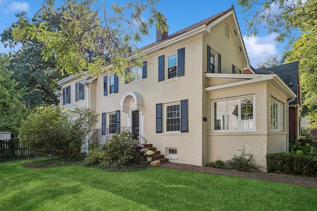 colonial inspired home with a front lawn, a chimney, and stucco siding