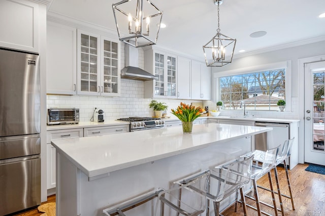 kitchen with white cabinets, wall chimney range hood, appliances with stainless steel finishes, and a breakfast bar