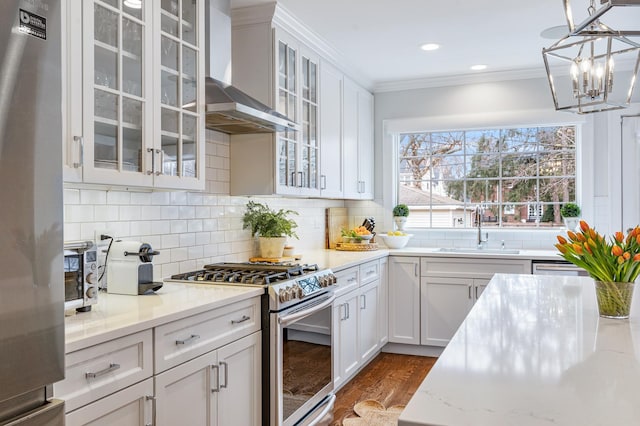 kitchen with tasteful backsplash, appliances with stainless steel finishes, ornamental molding, wall chimney range hood, and a sink