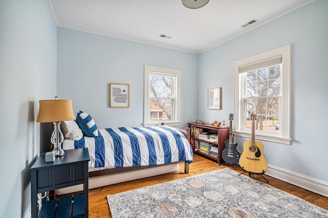 bedroom featuring visible vents, crown molding, baseboards, and wood finished floors