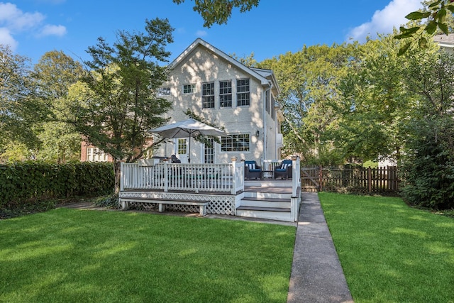 back of property with a lawn, a wooden deck, and fence