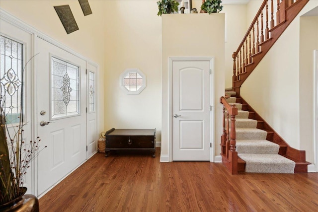 foyer entrance featuring a high ceiling, stairway, wood finished floors, and baseboards