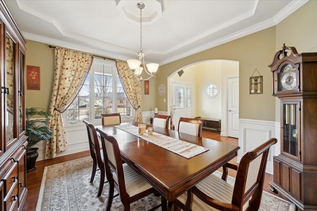 dining space with arched walkways, a raised ceiling, a notable chandelier, and wood finished floors