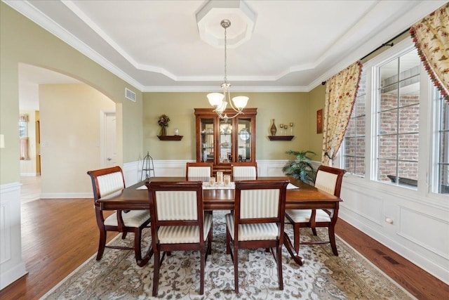 dining space with arched walkways, wood finished floors, visible vents, a raised ceiling, and an inviting chandelier