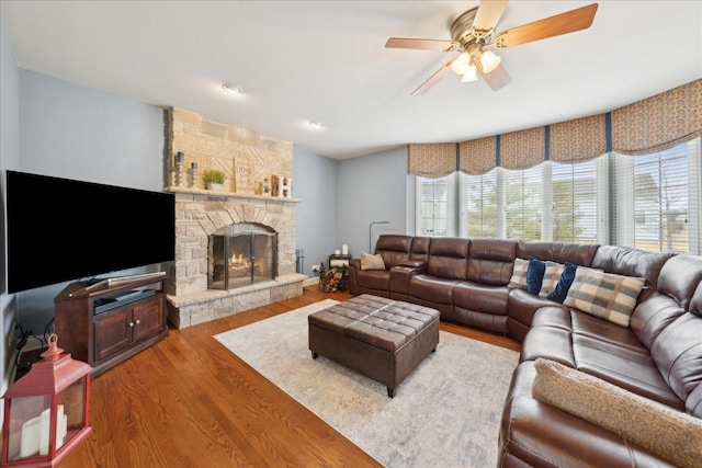 living area with a fireplace, wood finished floors, a wealth of natural light, and a ceiling fan