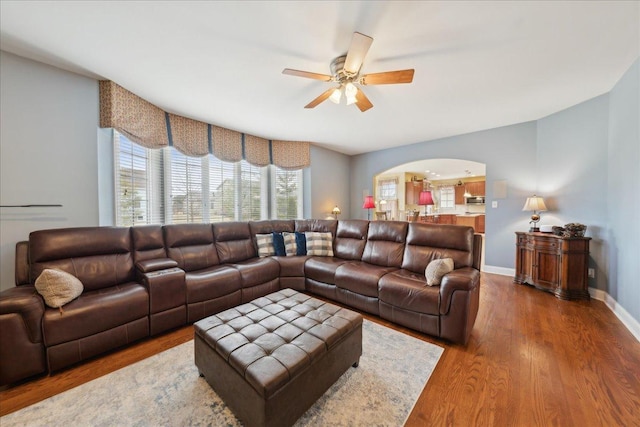 living area with arched walkways, ceiling fan, wood finished floors, and baseboards