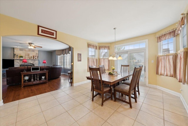 dining space with arched walkways, plenty of natural light, a stone fireplace, and light tile patterned floors