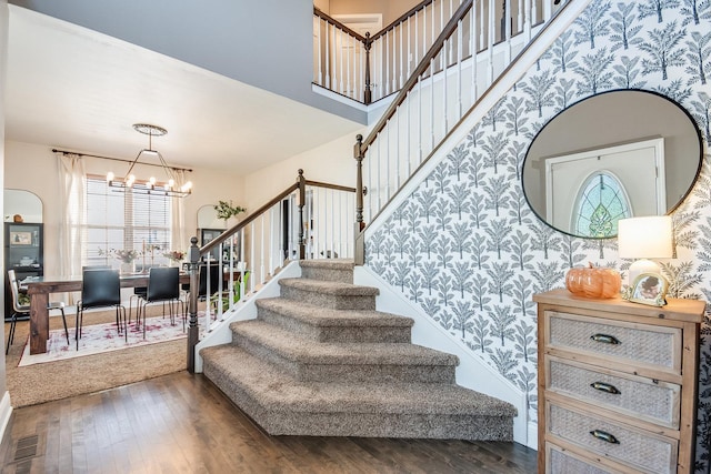 stairway featuring wood-type flooring, visible vents, a high ceiling, an inviting chandelier, and wallpapered walls