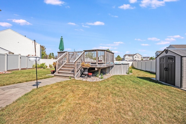 view of yard featuring a storage shed, a fenced backyard, a deck, and an outbuilding