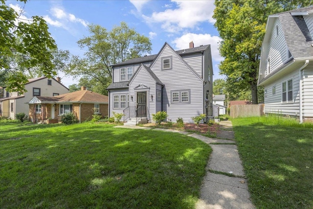 view of front facade with a chimney, a front yard, and fence