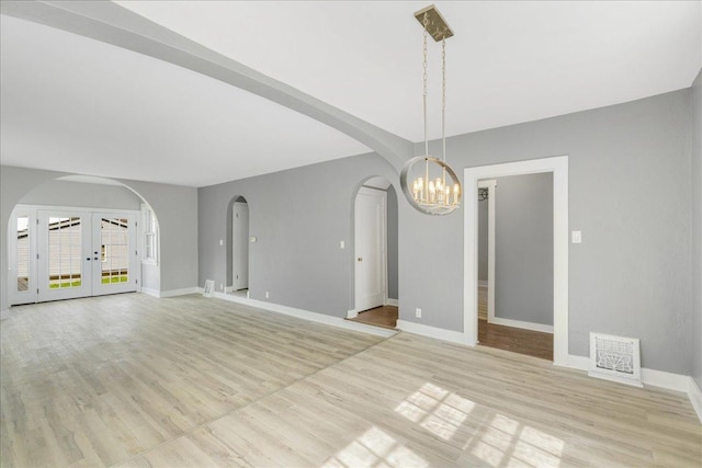 unfurnished living room featuring light wood-type flooring, baseboards, visible vents, and arched walkways