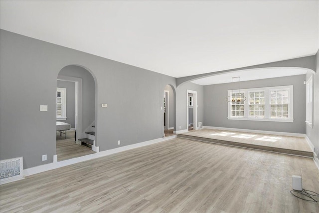 unfurnished living room featuring light wood-style flooring, visible vents, arched walkways, and baseboards