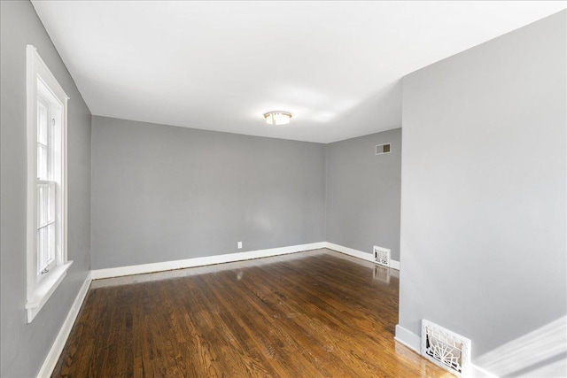 spare room with dark wood-style flooring, visible vents, and baseboards