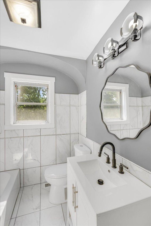 full bathroom with toilet, a bath, marble finish floor, vanity, and tile walls