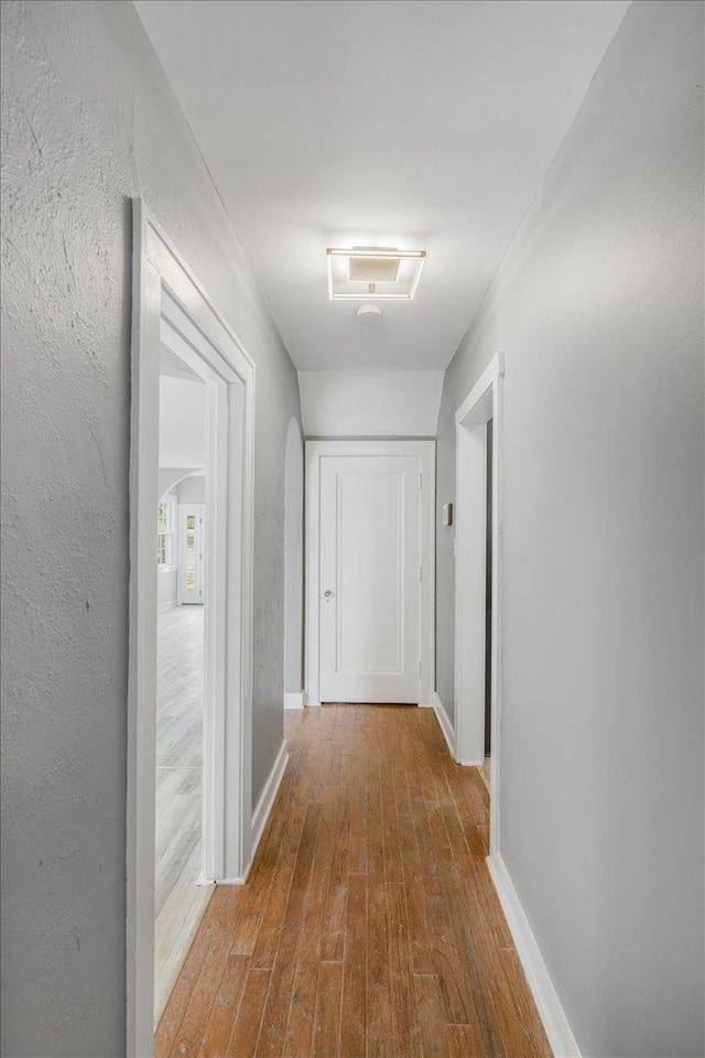 corridor with arched walkways, a textured wall, wood finished floors, and baseboards