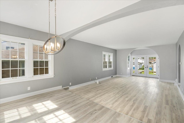 unfurnished living room featuring arched walkways, light wood-style flooring, visible vents, baseboards, and french doors