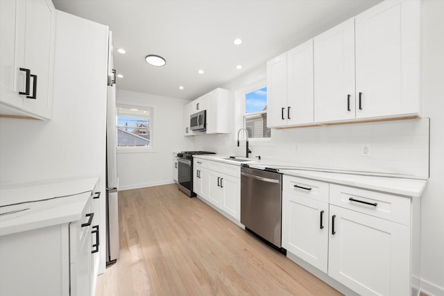 kitchen with appliances with stainless steel finishes, a wealth of natural light, light wood-style floors, and a sink