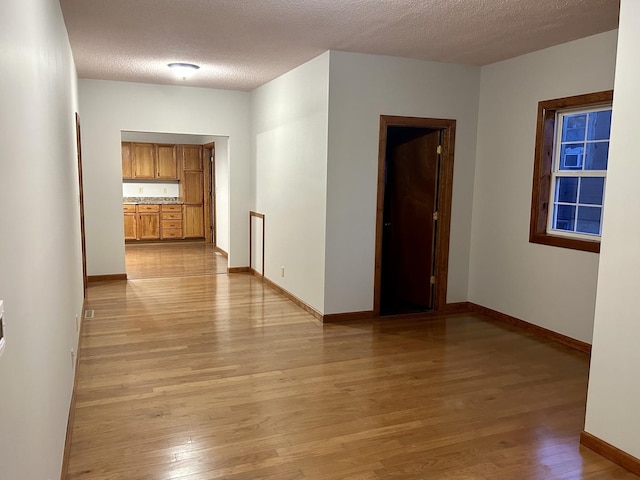 unfurnished room featuring light wood-style flooring, baseboards, and a textured ceiling