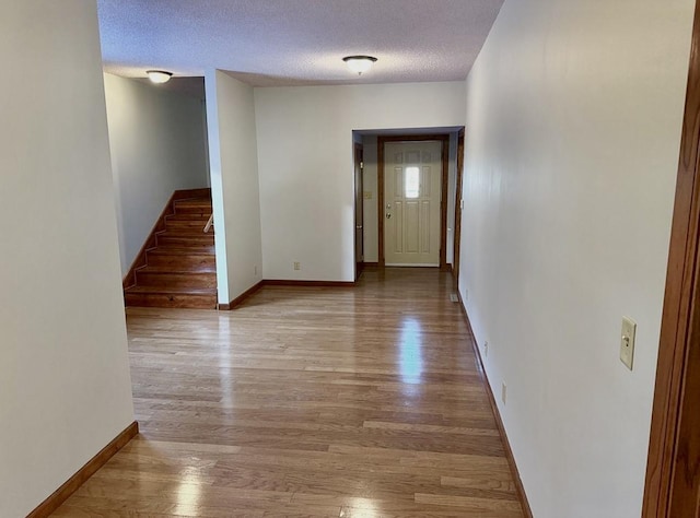 interior space with stairs, a textured ceiling, baseboards, and wood finished floors