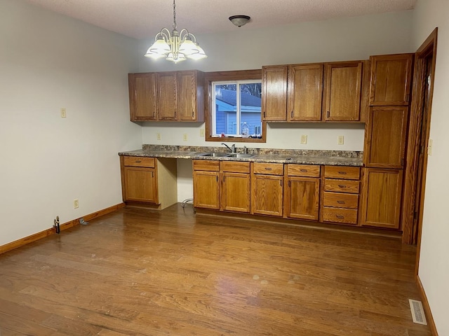 kitchen featuring dark wood-style flooring, brown cabinetry, a sink, and visible vents