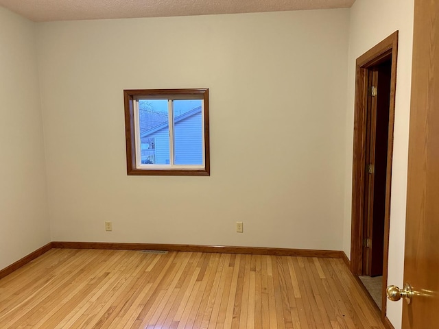 spare room featuring light wood-style flooring, baseboards, and a textured ceiling