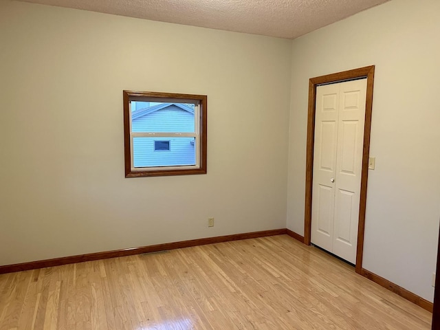 unfurnished room featuring light wood-type flooring, a textured ceiling, and baseboards