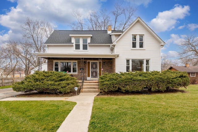 view of front facade featuring brick siding, roof with shingles, a chimney, and a front yard