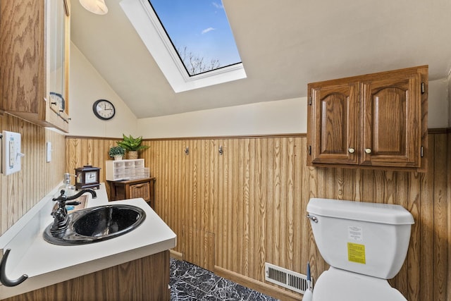 interior space featuring wooden walls, visible vents, lofted ceiling with skylight, a wainscoted wall, and a sink