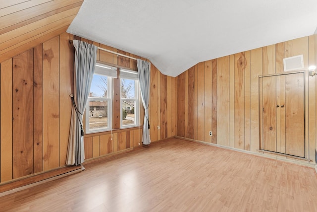 unfurnished room featuring lofted ceiling, wood walls, wood finished floors, and visible vents