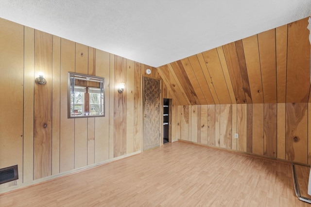 bonus room with lofted ceiling, wood walls, wood finished floors, and visible vents