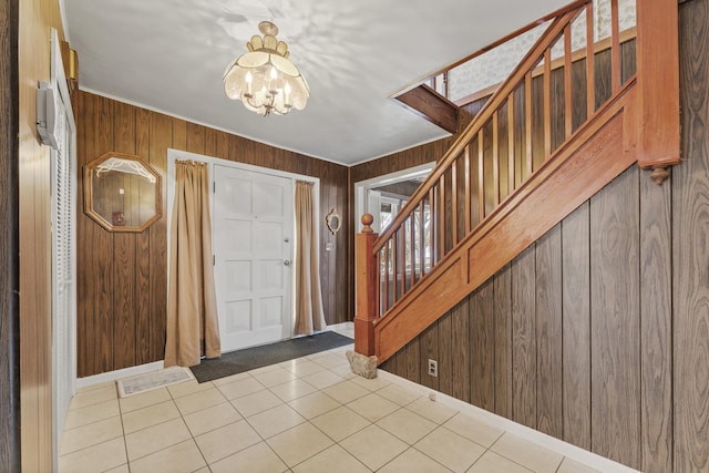 tiled foyer featuring a notable chandelier, wooden walls, baseboards, and stairs