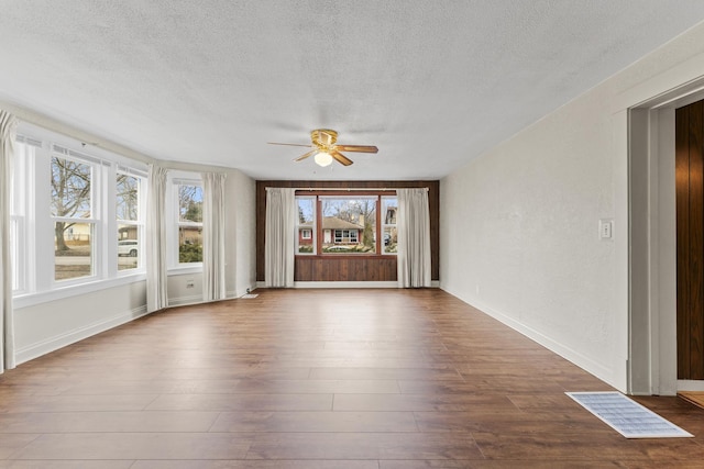 empty room featuring ceiling fan, a textured ceiling, baseboards, and wood finished floors