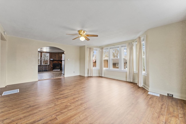 unfurnished living room featuring visible vents, arched walkways, ceiling fan, wood finished floors, and a fireplace