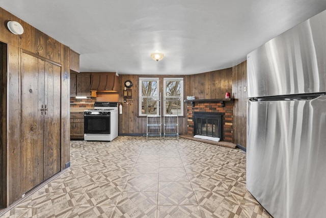 kitchen featuring wooden walls, gas range, freestanding refrigerator, light floors, and a fireplace