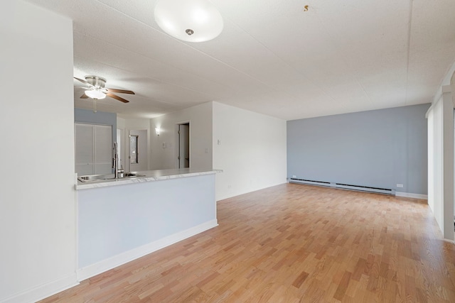 unfurnished living room with light wood finished floors, a baseboard radiator, a sink, ceiling fan, and baseboards