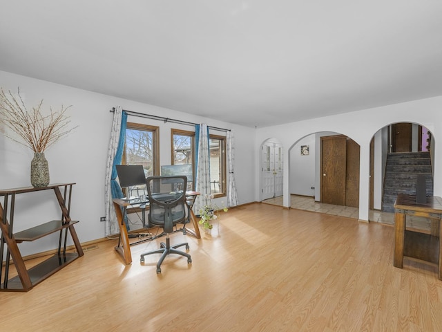 office area featuring baseboards, arched walkways, and wood finished floors