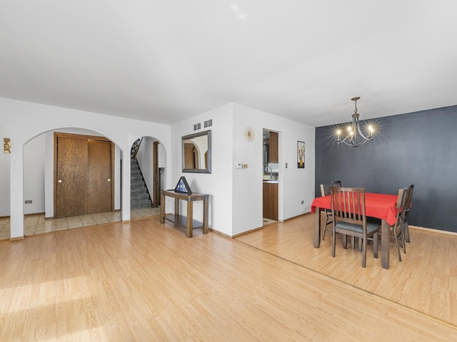 dining space with arched walkways, light wood finished floors, visible vents, stairway, and an accent wall