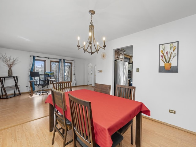 dining area with arched walkways, light wood finished floors, an inviting chandelier, and baseboards