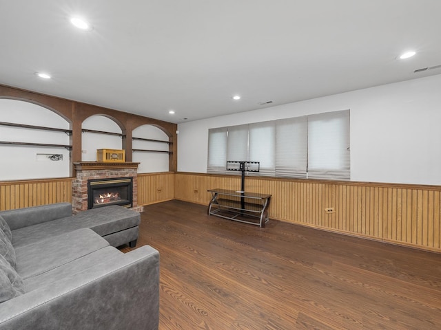 living area featuring a brick fireplace, visible vents, wood finished floors, and wainscoting