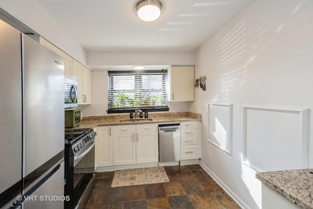 kitchen with a sink, stone finish flooring, baseboards, appliances with stainless steel finishes, and light stone countertops