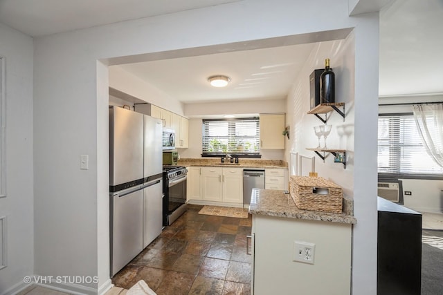 kitchen with a sink, stone tile flooring, stainless steel appliances, baseboards, and light stone countertops